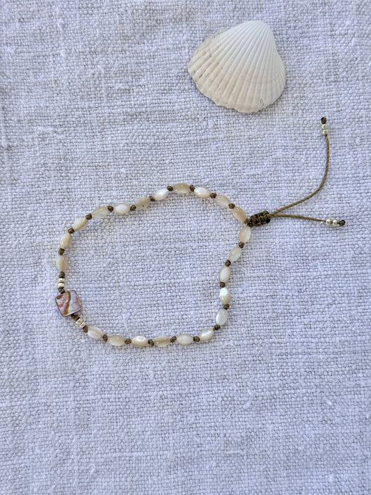 Bracelet Lichen en entier, nacres beige nouées sur cordon olive et carré de nacre abalone, posé sur du lin avec un coquillage — fait main en Normandie