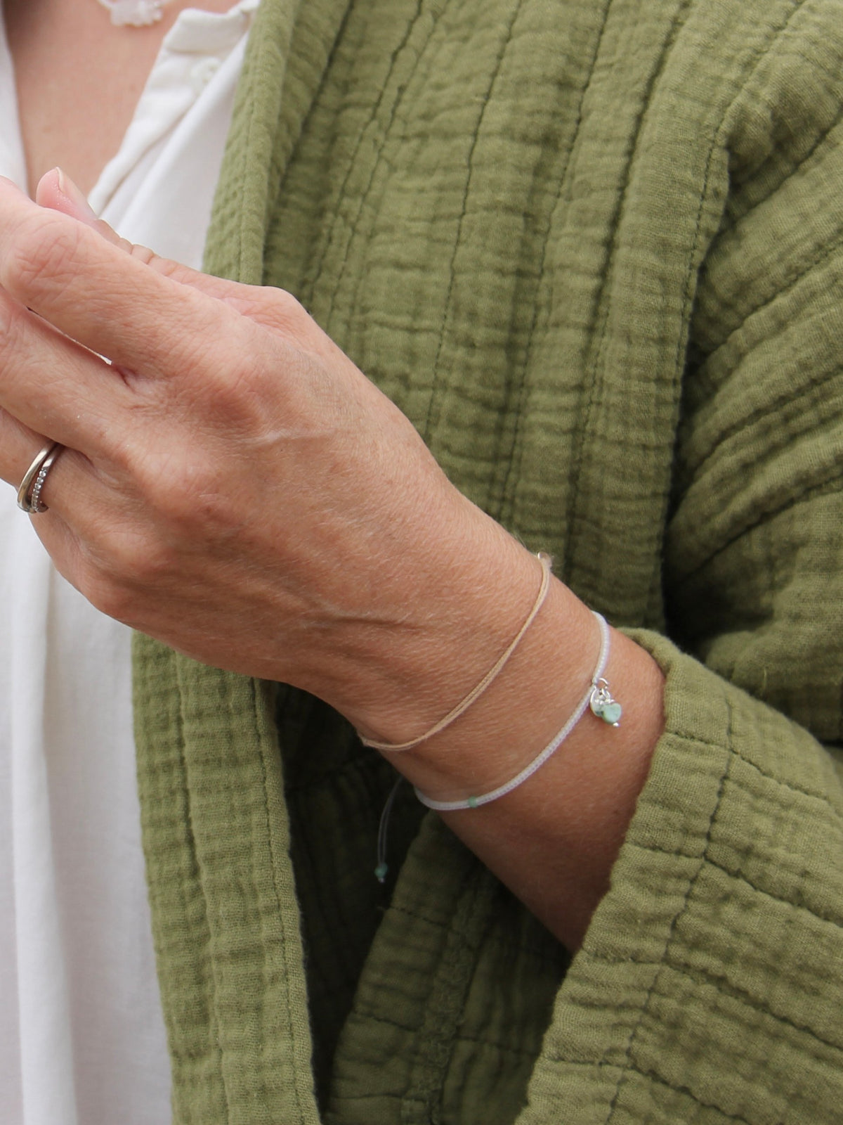 Bracelet Brume porté avec une veste vert olive, perles cristal, cœur en turquoise et médaille argent 925 — fait main en Normandie