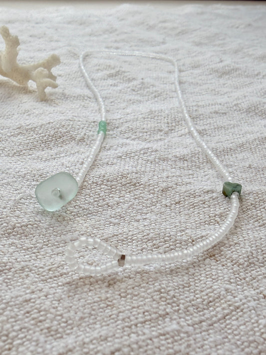 Collier lasso Brume en perles cristal mat, verre de mer et cœur en pierre verte, posé sur du lin