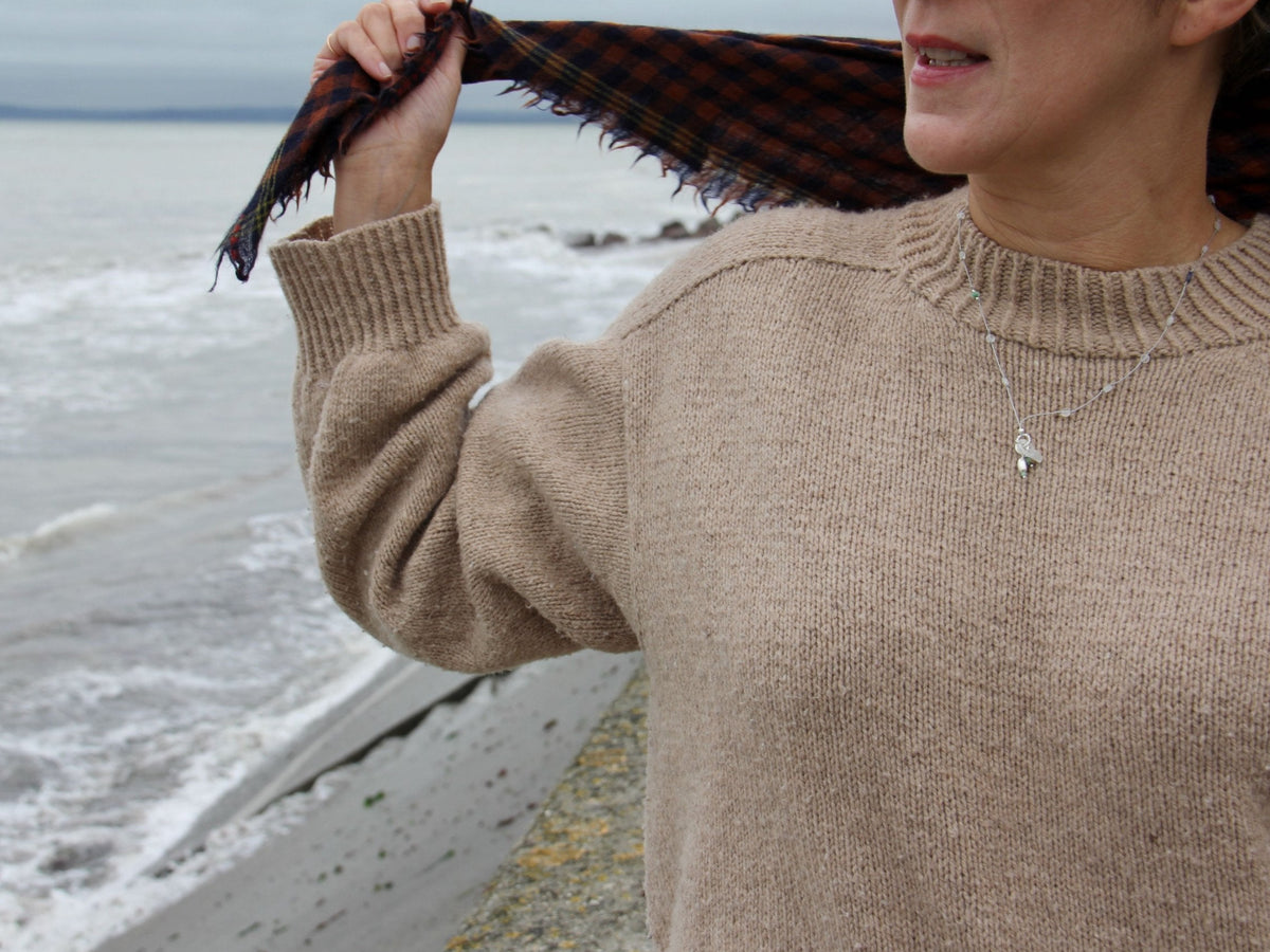 Collier long Brume en pierre de lune et argent 925, porté sur un pull beige au bord de la mer