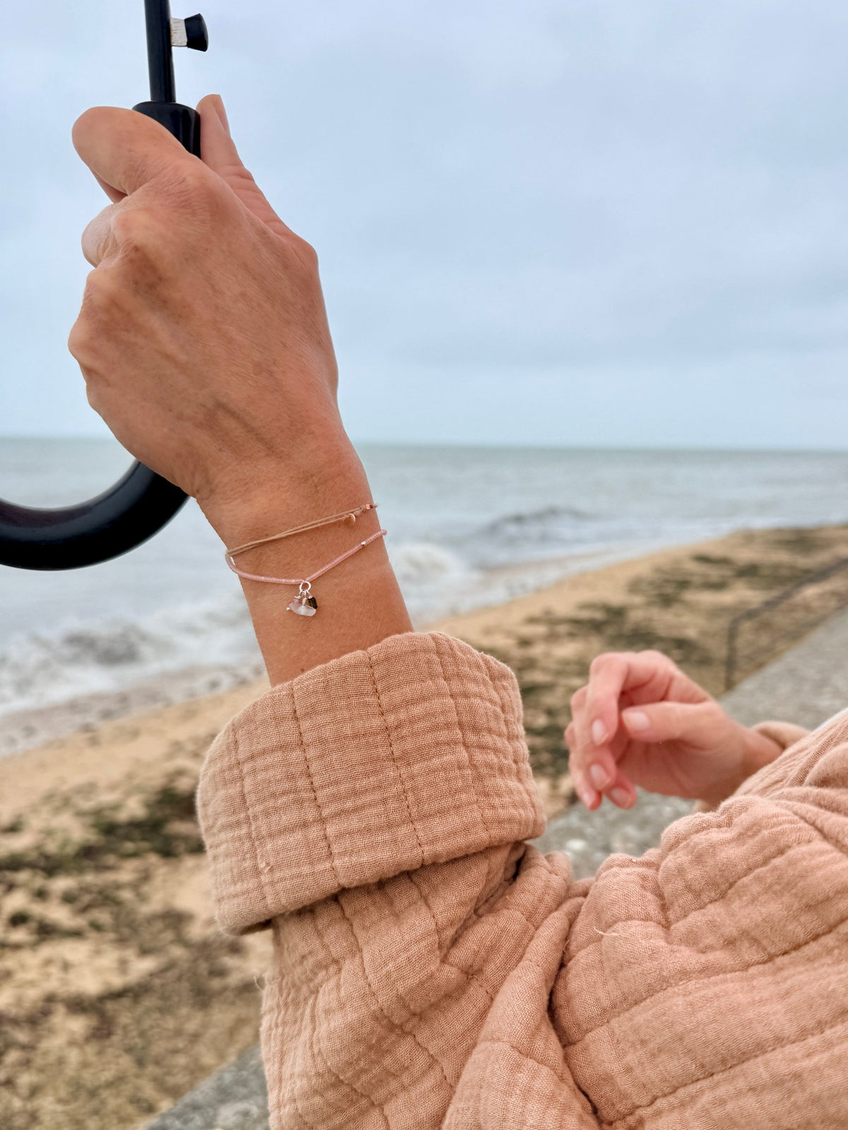 Bracelet Bruyère porté au poignet sur la digue, petites breloques tourmaline et verre de mer — fait main en Normandie