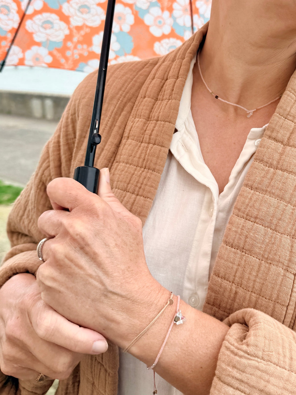 Collier et bracelet Bruyère portés avec une veste camel sous un parapluie fleuri