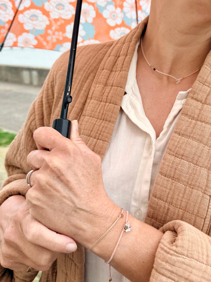 Collier et bracelet Bruyère portés avec une veste camel sous un parapluie fleuri