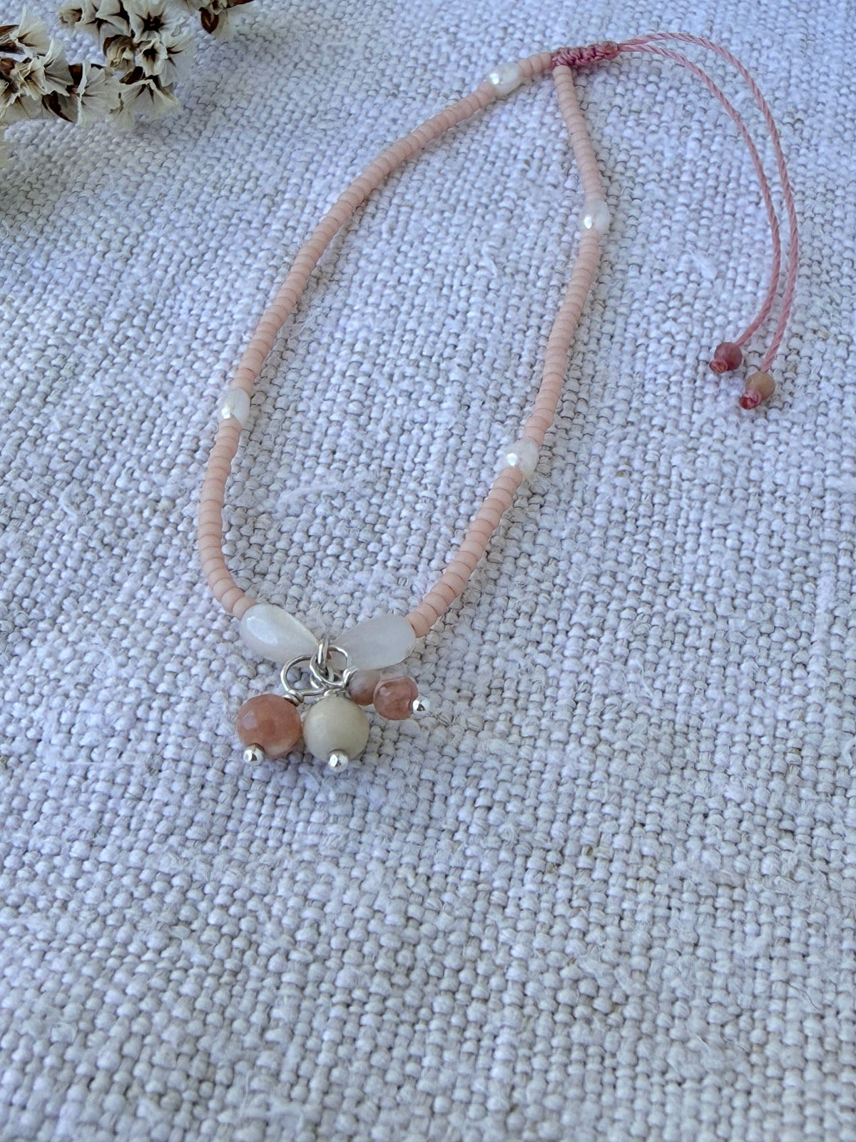 Bracelet Dune posé sur du lin près de fleurs séchées, perles rose poudré, nacre et grappe de rhodochrosite