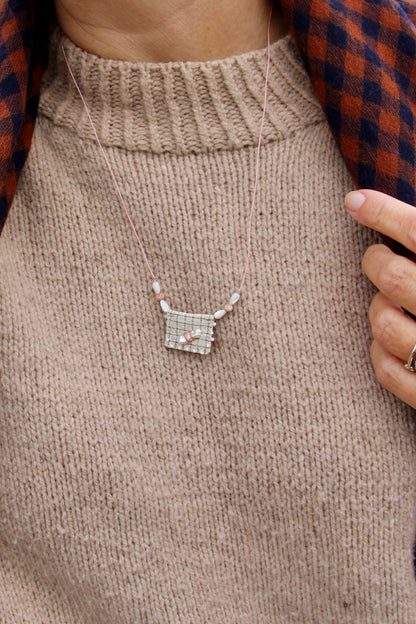 Collier long brodé Dune porté sur un pull beige, médaille en tissu à carreaux, nacre baroque et rhodochrosites sur cordon rose — fait main en Normandie