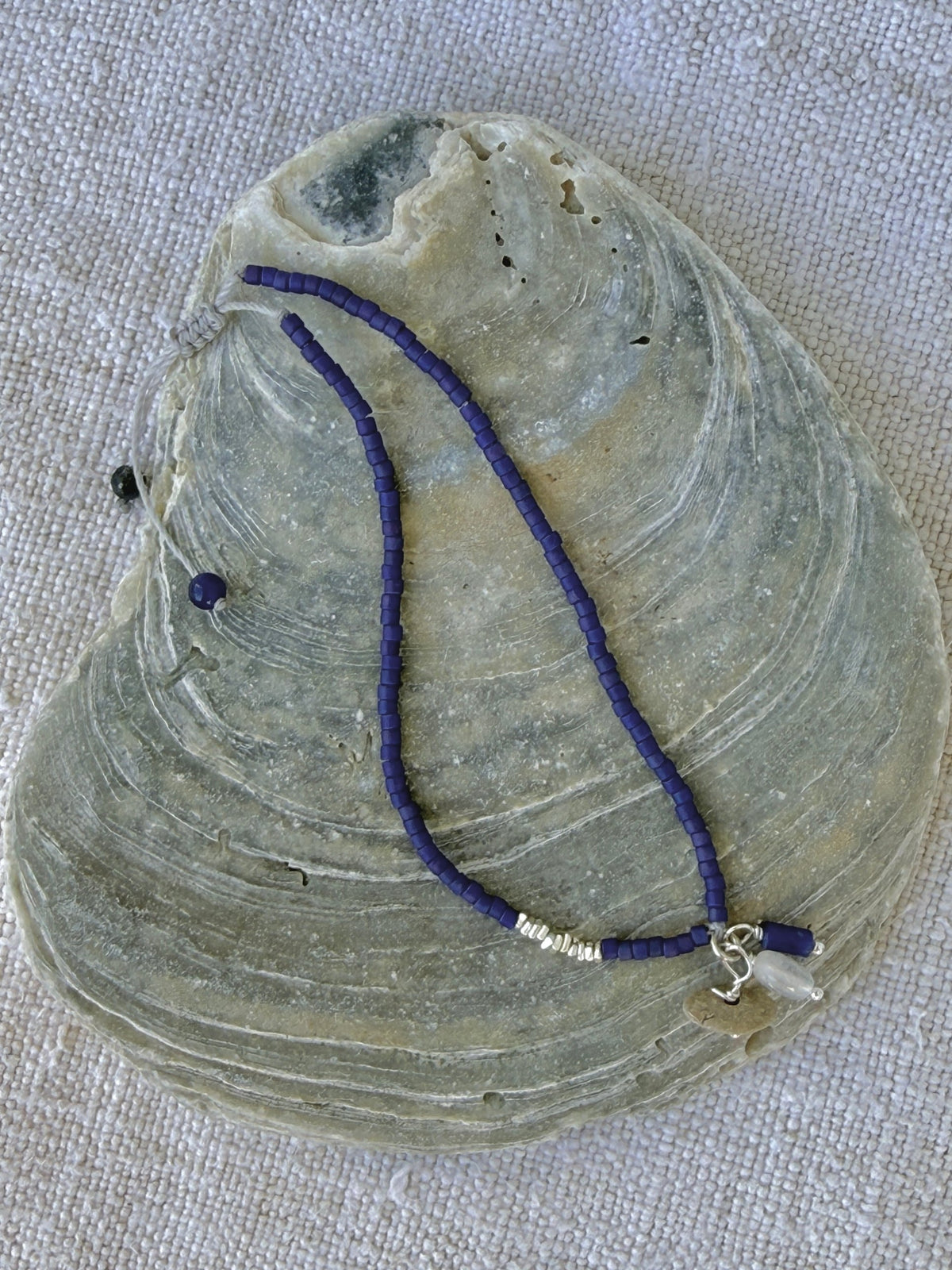 Bracelet Embrun en entier posé sur une coquille d'huître, perles indigo mat, perles argent et breloques galet, pierre de lune et sodalite — fait main en Normandie