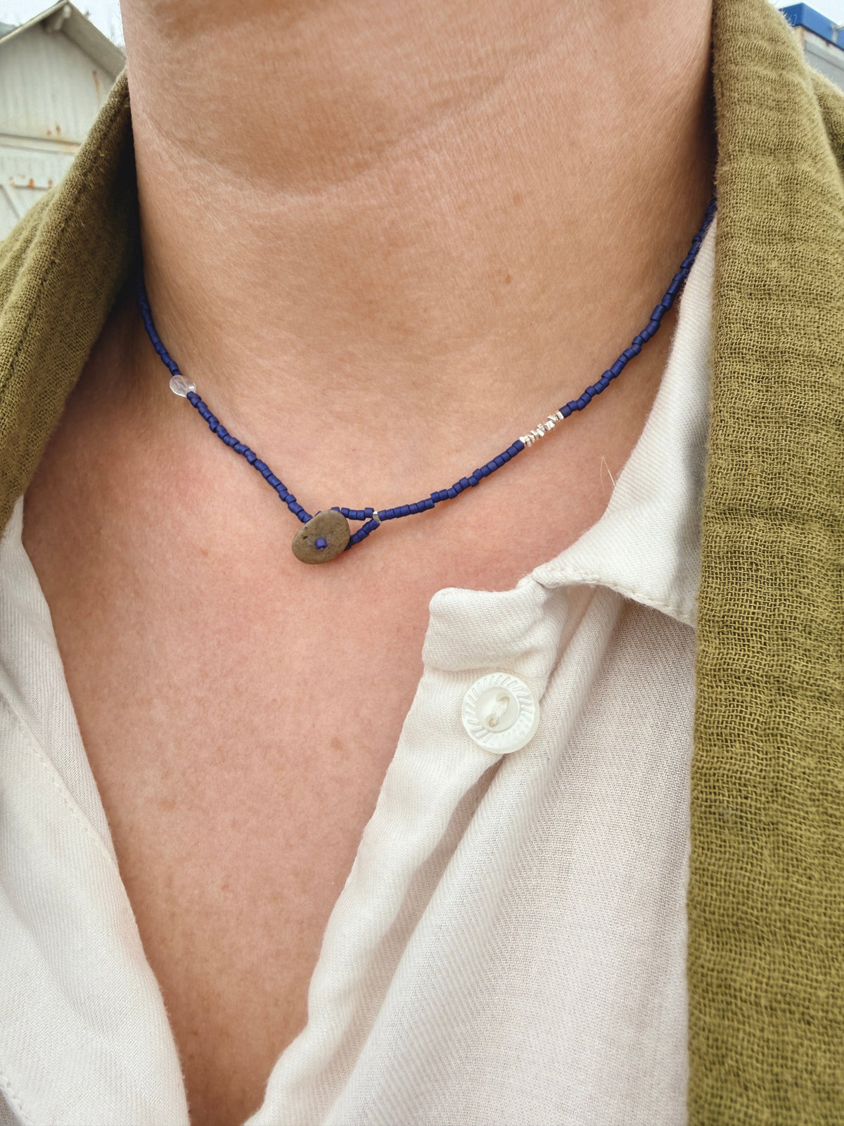 Collier court Embrun porté sur une chemise blanche, perles indigo, pierre de lune et galet