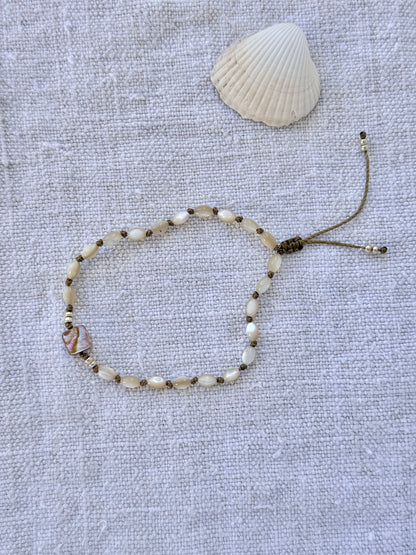 Bracelet Lichen en entier, nacres beige nouées sur cordon olive et carré de nacre abalone, posé sur du lin avec un coquillage — fait main en Normandie