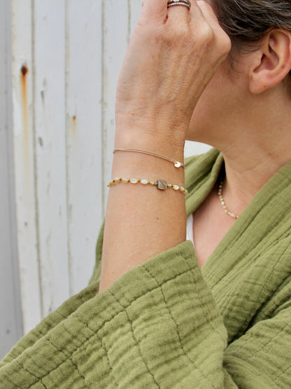 Bracelet Lichen porté devant une porte blanche, nacres olive nouées et carré de nacre d'ormeau