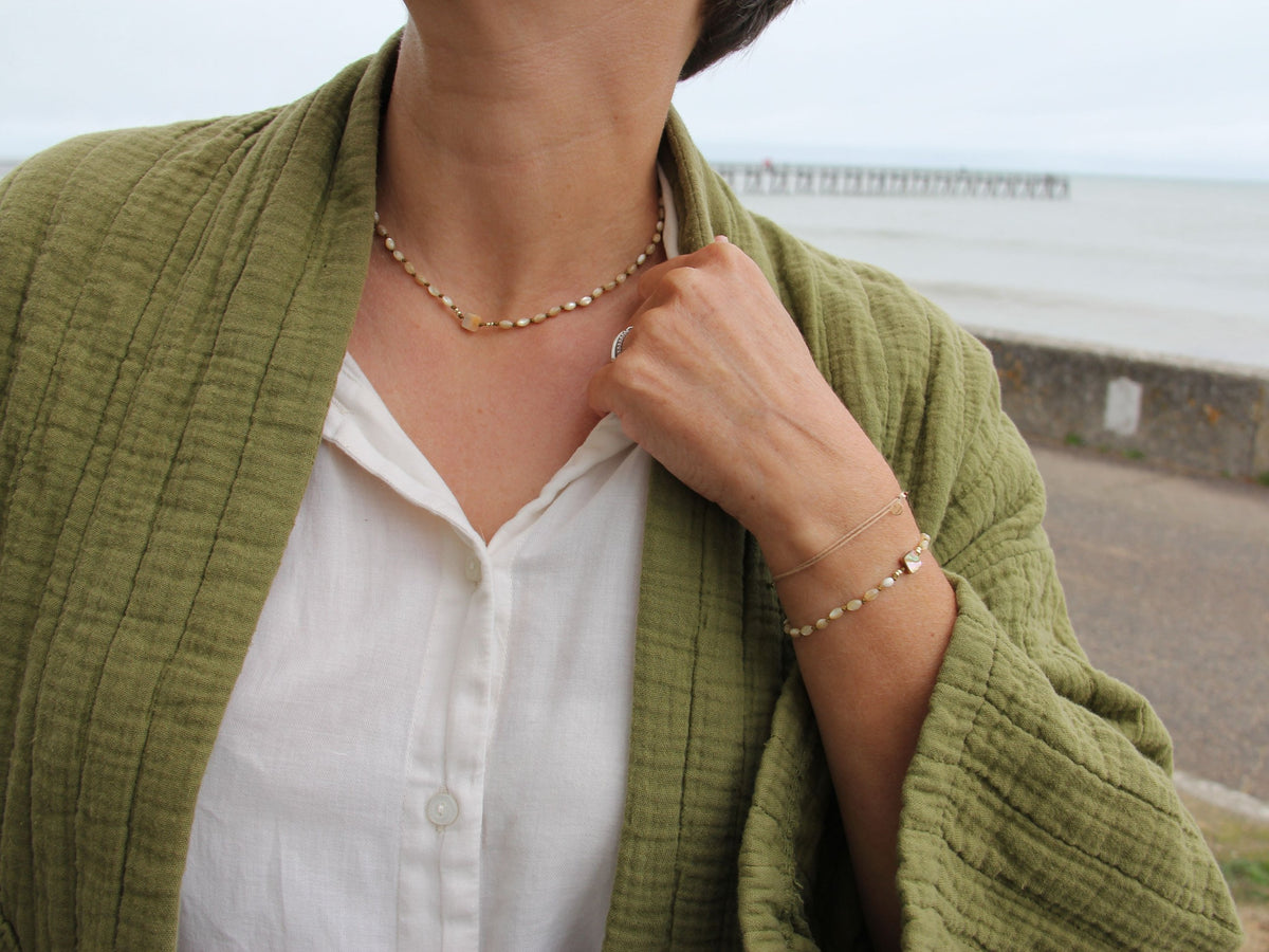 Collier et bracelet Lichen portés avec une veste vert olive face à la mer