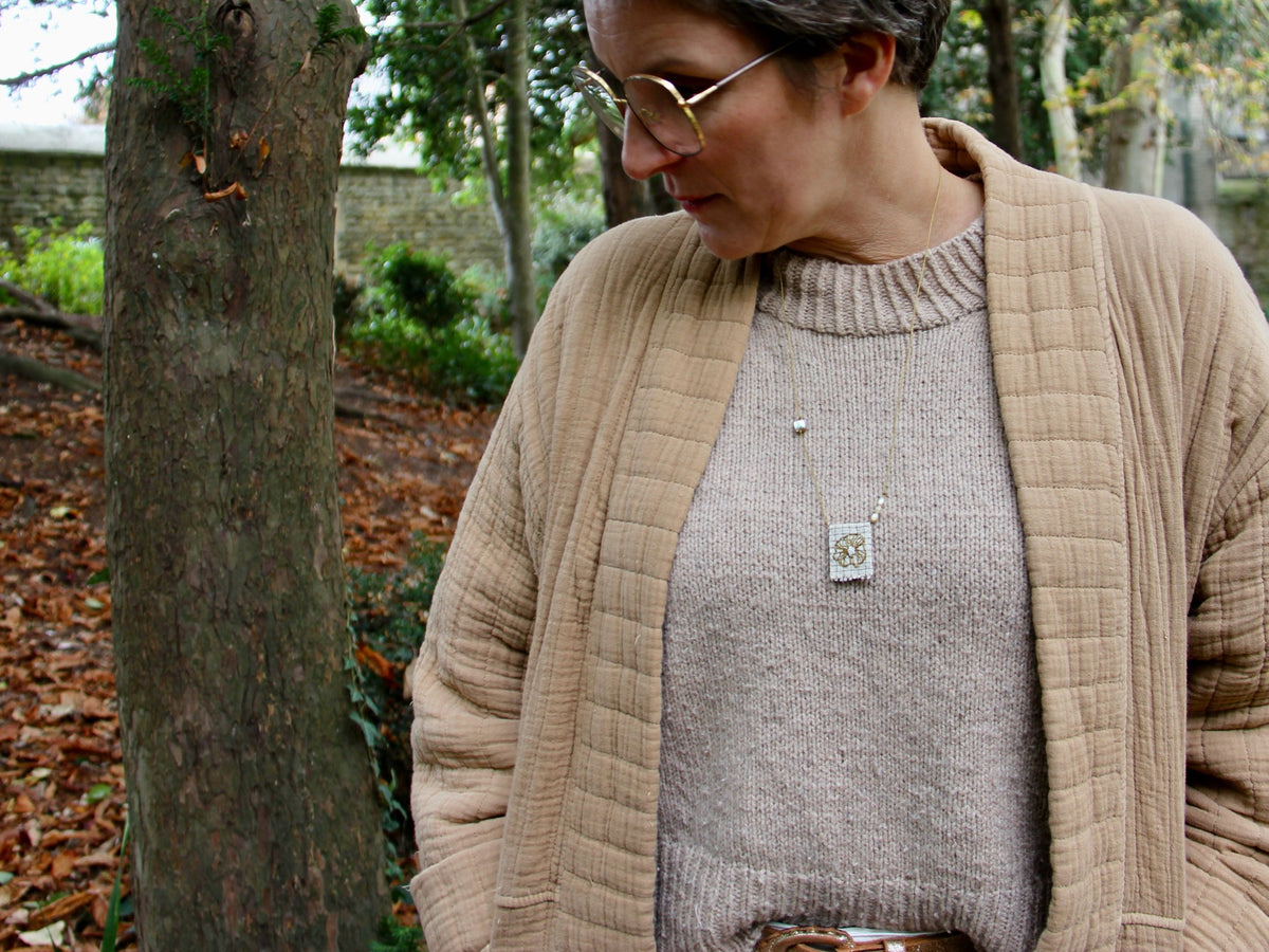 Collier Lichen médaille brodée porté sur un pull beige dans un jardin d'automne