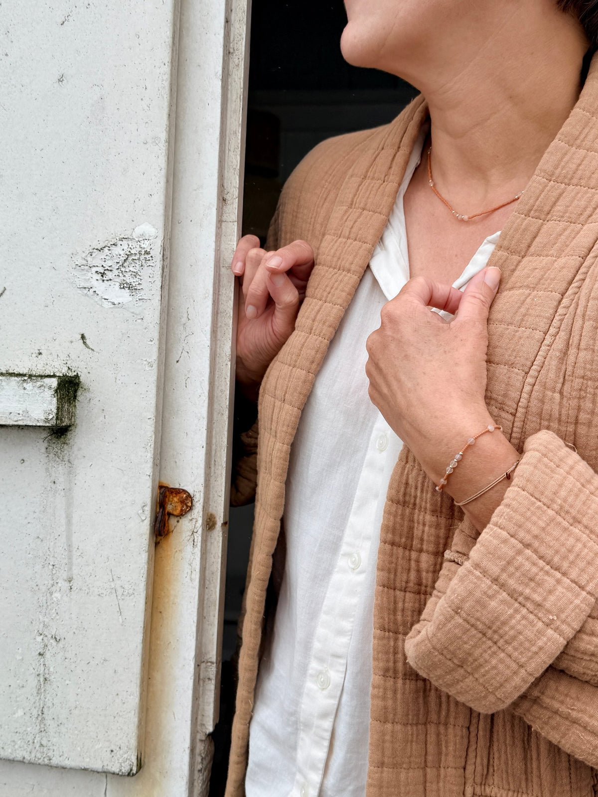 Collier et bracelet Tarte aux Pommes portés sur une chemise blanche, devant une cabine de plage