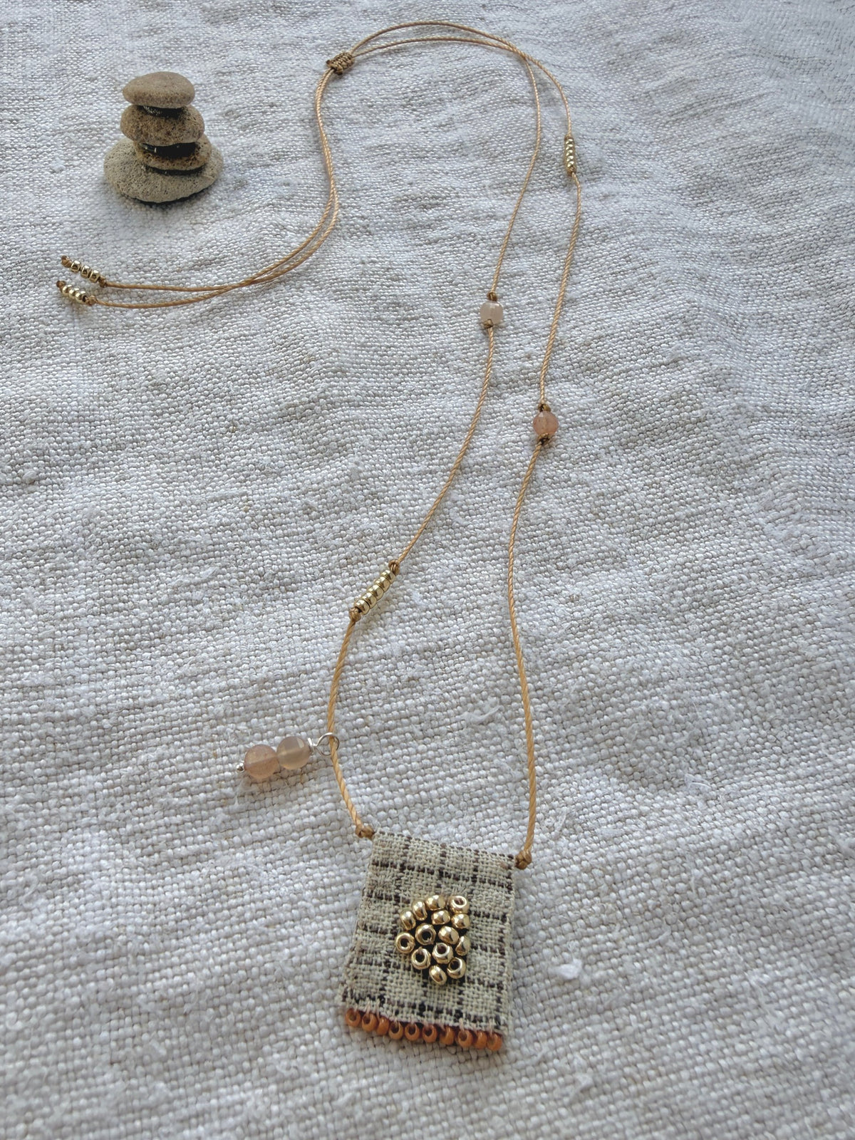 Collier long brodé Tarte aux Pommes posé sur du lin, médaille à carreaux, perles dorées et pierres de lune pêche