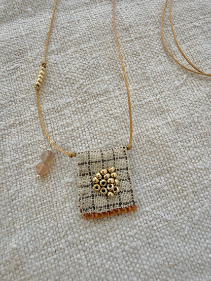 Gros plan sur la médaille Tarte aux Pommes : tissu à carreaux brodé de perles dorées, franges orange cuit et pampille de pierres de lune pêche