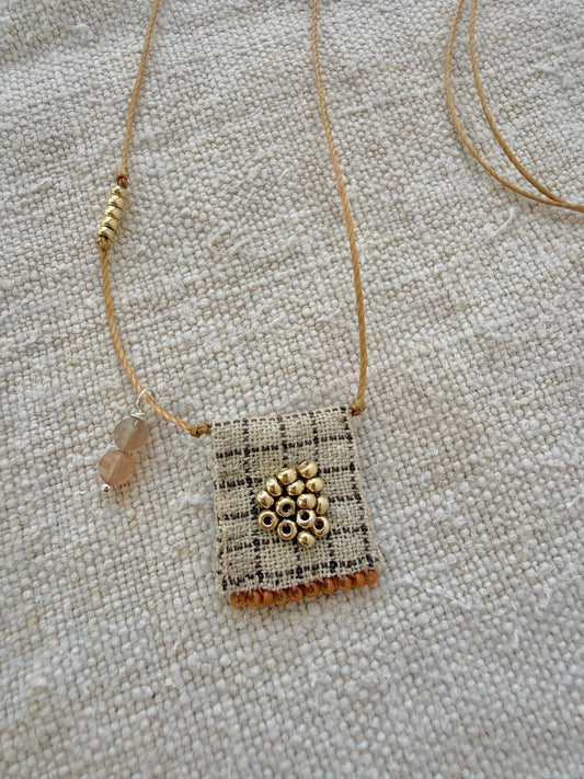 Gros plan sur la médaille Tarte aux Pommes : tissu à carreaux brodé de perles dorées, franges orange cuit et pampille de pierres de lune pêche